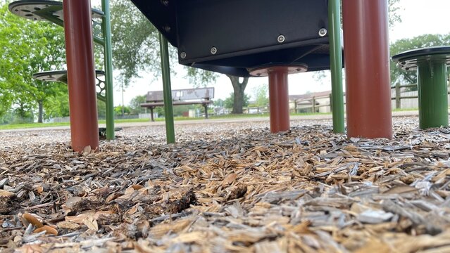 Low angle view beneath playground equipment with red support posts black platform and wood chip mulch showing shaded recreational structure details safety surfacing and quiet park environment