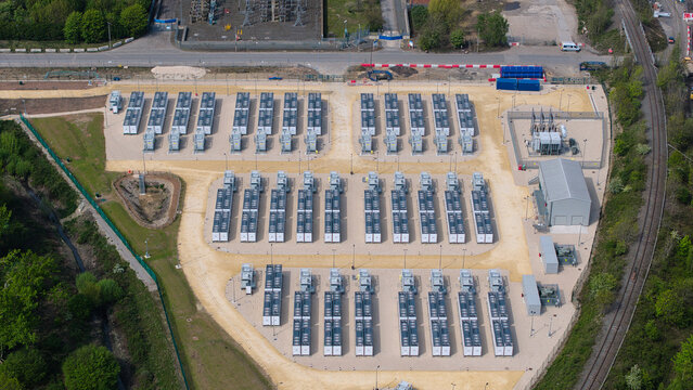 Aerial view of Battery Energy Storage Systems with rows of industrial containers and electrical infrastructure surrounded by green trees in Knottingley, England, United Kingdom.