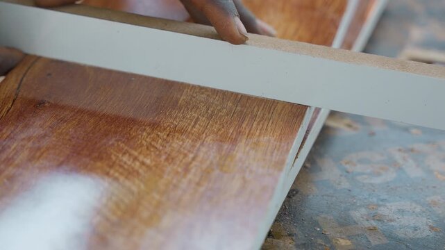 Closeup of carpenter smoothing plank edge, sanding glossy hardwood board on bench with hand tool, light dusting of sawdust and deliberate, precise strokes highlighting craftsmanship and surface