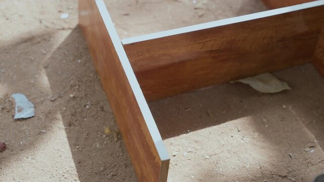 Closeup of carpenter assembling wooden frame corner on dusty worksite, aligning joint by hand and checking fit under sunlight, practical furniture build conveying steady skill and measured placement.