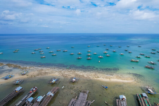 Wide aerial landscape of a tropical coastline featuring wooden fish drying piers in and dozens of floating aquaculture platforms stretching towards the horizon in Tanjung Binga, Belitung, Indonesia.