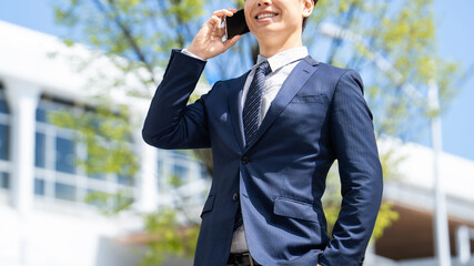 オフィス街でスマートフォンで話す日本人男性ビジネスパーソンのビジネスイメージ, Japanese Businessman Talking on Smartphone in Office District © Trickster*