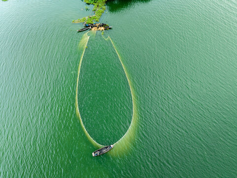 Aerial view of fishermen in wooden boats casting a large oval net on the green waters of Kaptai Lake in Rangamati, Chittagong Division, Bangladesh.
