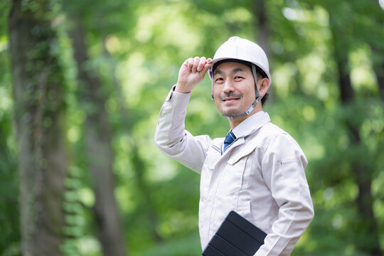 公園などでヘルメット姿でタブレットで点検する林業や施工管理などの現場作業員のポートレート安全管理とDX業務　カメラ目線上半身クローズアップ