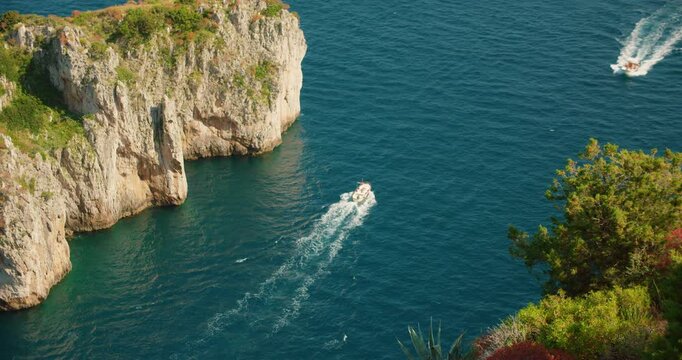 A tour boat glides along the rocky coastline of Capri Italy on a calm sunny summer day