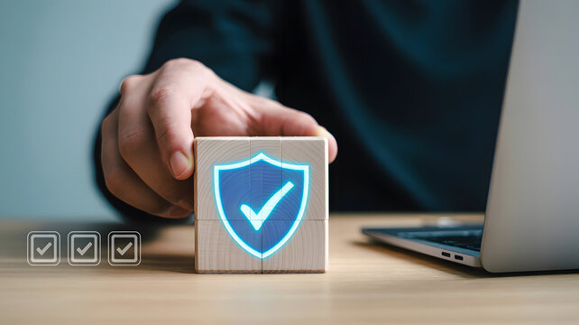Close-up shot of a hand placing a wooden block with a shield icon symbolizing security and protection, checkmarks in the background
