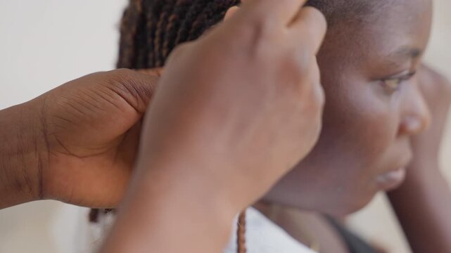 Closeup hair braiding with comb and hands, quiet studio mood. Stylist gently weaves cornrows along clients scalp, slow focused technique, tactile detail and patient craft, close profile shot