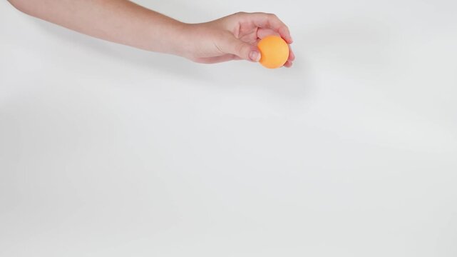 A hand drops an orange ping pong ball on white background, showcasing its bounce and movement in slow motion. The ball&rsquo;s dynamic trajectory captures attention against the clean, bright backdrop.