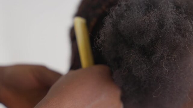 Closeup black stylist detangling dense afro hair using yellow comb, precise sectioning along scalp in neutral studio, skilled hands executing patient grooming technique with focus on texture and tool