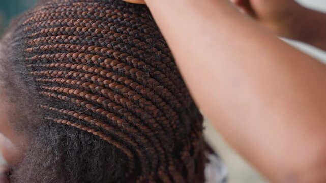 Professional hairstylist crafting neat cornrows. Calm salon environment with meticulous hairstyling methods. Closeup of stylist carefully forming precise side cornrow hairstyles with gentle hands