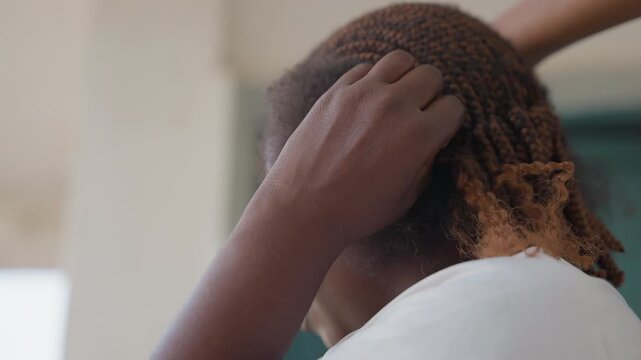 Black woman braid maintenance closeup hands combing scalp adjusting braids in calm community salon trainee stylist separating sections with gentle fingers natural light textured ends patient routine