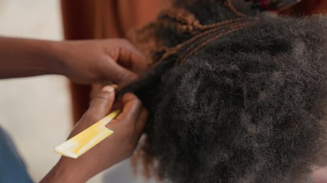 Closeup hands parting natural hair, stylist sections tight coils with finetooth comb preparing neat cornrow braids, intimate home salon scene with slow deliberate movements gentle tension focused