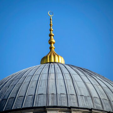 Close-up of a mosque's dome and golden crescent finial against a clear, brilliant blue sky, symbolizing faith and architecture