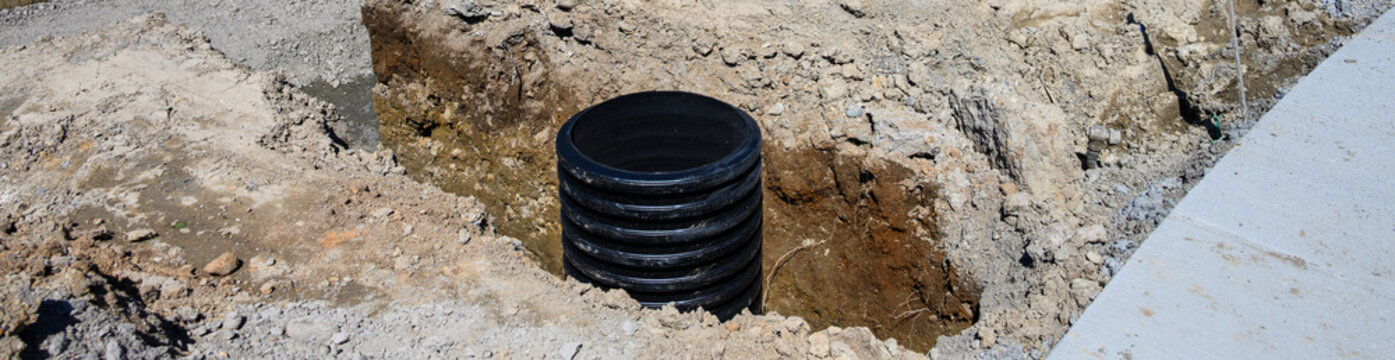 Septic Tank Riser, large black plastic corrugated pipe, installed in trench dug out in dirt of housing development construction project, site preparation detail earthwork
