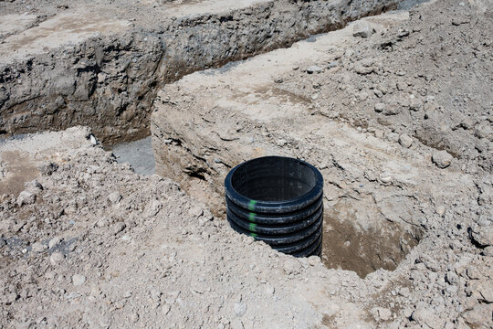 Septic Tank Riser, large black plastic corrugated pipe, installed in trench dug out in dirt of housing development construction project, site preparation detail earthwork
