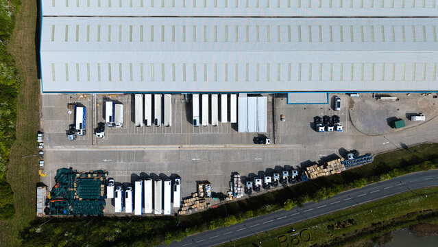 Aerial view of a large BQ industrial warehouse with white semi-truck trailers parked at loading docks and cargo containers in a logistics hub in Doncaster, England, United Kingdom.