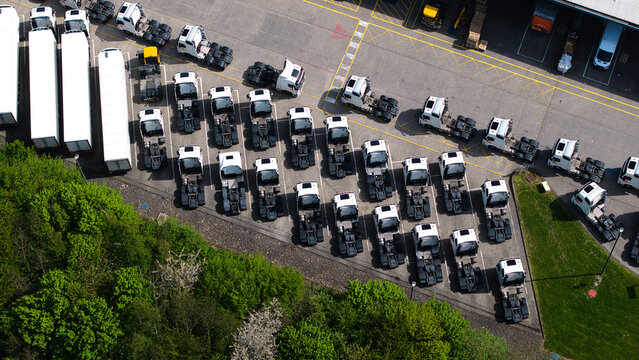Aerial view of white semi-truck cabs parked in neat rows at a logistics depot next to a green forest Doncaster, England, United Kingdom.