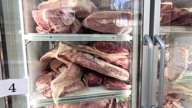Camera tilting up to show variety of premium wagyu beef cuts inside commercial refrigerator at butcher shop.