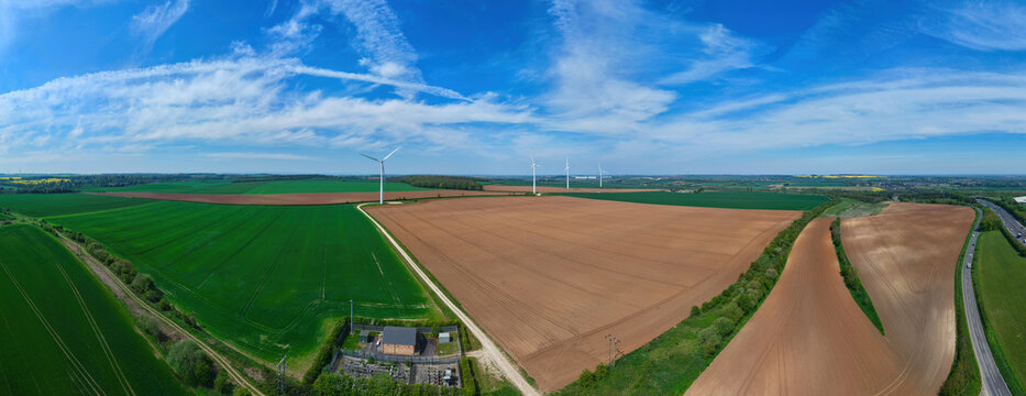 Aerial view of vast agricultural fields with wind turbines under a blue sky with wispy clouds near Hampole, England, United Kingdom.