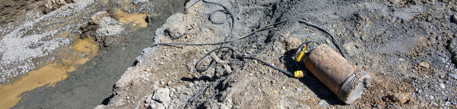 Submersible pump with power cord used to pump water out of trenches dug on construction site, laying on ground ready to use
