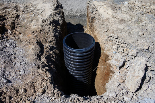 Septic Tank Riser, large black plastic corrugated pipe, installed in trench dug out in dirt of housing development construction project, site preparation detail earthwork
