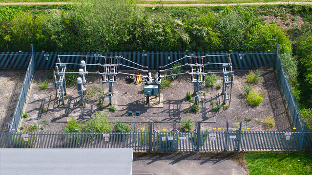 Aerial view of an electrical substation with transformers and power lines enclosed by a metal fence surrounded by green trees in Hampole, England, United Kingdom.