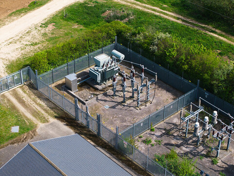Aerial view of an electrical substation with transformers and power equipment enclosed by a metal fence and green bushes in Hampole, England, United Kingdom.