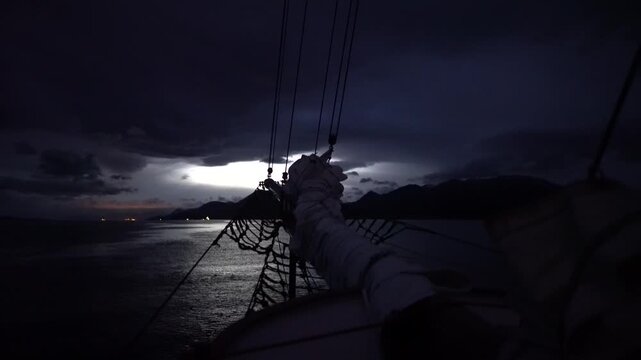 Cinematic night POV from the deck of the schooner Amazone as it navigates the dark, calm waters of the Beagle Channel, with the silhouetted Andes Mountains of Tierra del Fuego in the background