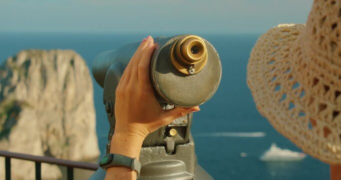Tourist using telescope to observe Capri seascape and Faraglioni rock formations