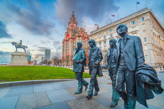 The Beatles Statue stands at Pier Head in front of the illuminated Port of Liverpool Building during twilight.