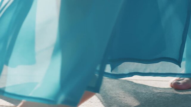 Bare feet on pavement and deck, woman in flowing blue dress, gentle steps over stone and grass edge, sunlight casting soft shadows, closeup toes and sheer fabric motion, calm weekend park mood