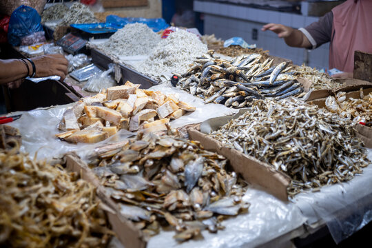 Various types of ikan asin (salted dried fish) displayed in cardboard boxes and trays at a traditional market stall in Jakarta, showing preserved seafood commonly sold for daily cooking ingredients.