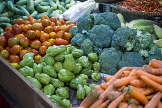 Fresh vegetables including labu siam, broccoli, tomatoes, carrots, cucumbers, and corn arranged at a traditional market in Jakarta, showing colorful local produce sold for daily cooking needs.