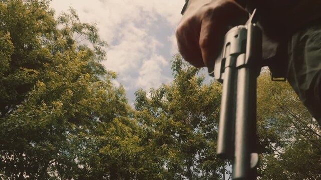Cowboy walks by holding a revolver handgun, with trees in background. Shot from a low angle at a high frame rate and edited in classic vintage western film style.