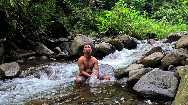 An Asian man bathes in a river in the middle of a beautiful forest