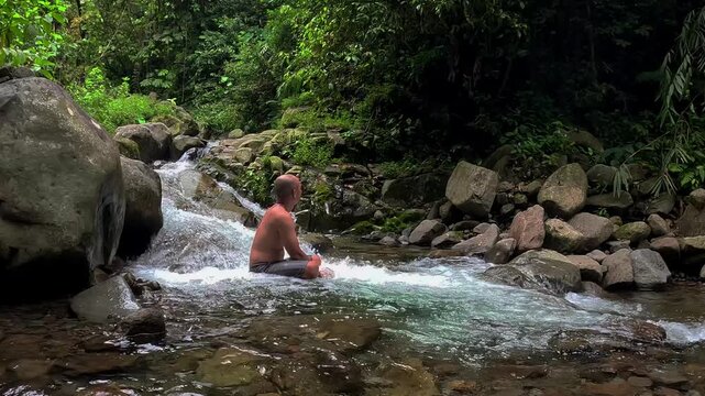 An Asian man bathes in a river in the middle of a beautiful forest