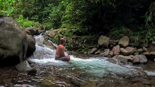 An Asian man bathes in a river in the middle of a beautiful forest