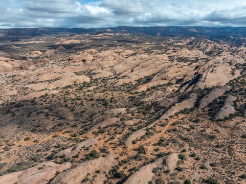 Aerial view of rolling sandstone rock formations and sparse desert vegetation under a partly cloudy sky.