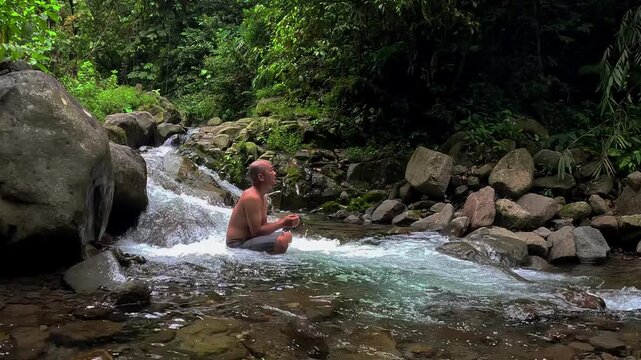 An Asian man bathes in a river in the middle of a beautiful forest