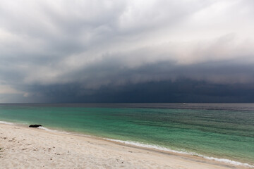 Fototapeta premium Koh Adang shoreline. Turquoise Andaman Sea meeting white sand. Low storm clouds approach over the water. Tarutao National Marine Park, Thailand.
