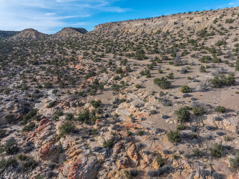 Aerial view of rugged desert hills with sparse green shrubs and rocky terrain under a blue sky.
