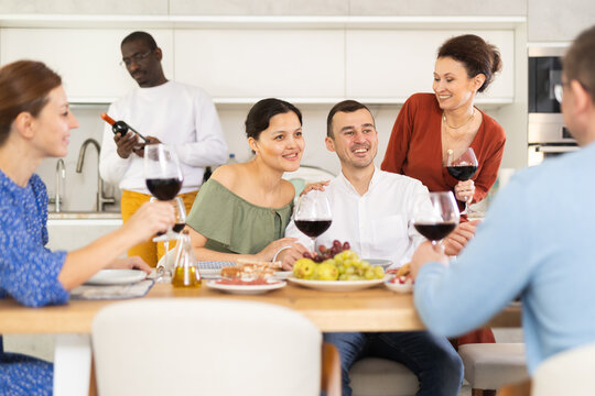 Multicultural female and male friends chatting and drinking wine at table