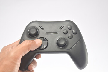 hand holding a black wireless gamepad controller isolated on a white background. Modern gaming hardware featuring dual analog sticks, directional pad, and action buttons for console or pc. © Setyotuhu