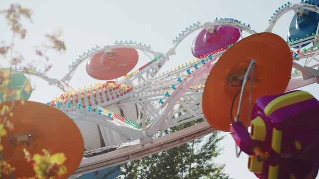 Colorful amusement ride at park, sunlit spinning gondolas and umbrella seats convey family weekend atmosphere with bright lights, gentle motion, leafy trees, lowangle sky backdrop, festive carnival