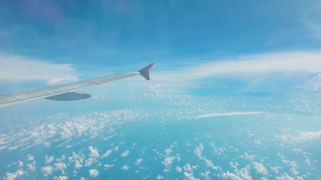 Experience the serene beauty of a clear blue sky filled with fluffy white clouds from the perspective of an airplane wing. This tranquil aerial view captures the essence of travel and freedom,