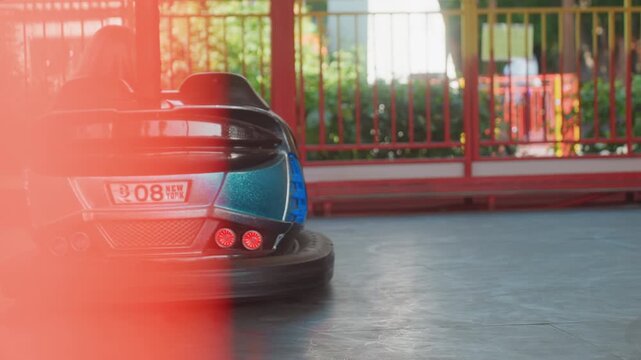 Young driver racing teal bumper car, red light leak and motion blur, energetic park weekend scene with family cheering, closeup rear angle showing steering and speed, candid fastpaced amusement ride