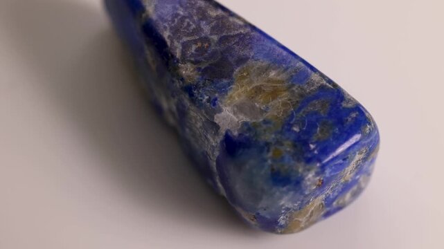 Close up cinematic shot of lapis lazuli stone rotating on white background, shiny mineral texture with rich blue color.