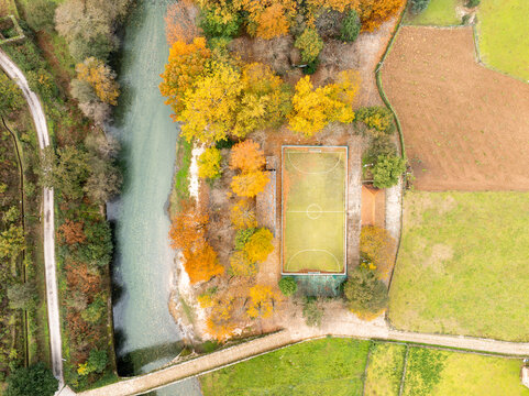 Aerial view of Praia Fluvial de Alvoco das Varzeas with a soccer field nestled among colorful autumn trees and the Alvoco River in Alvoco das Varzeas, Coimbra, Portugal.