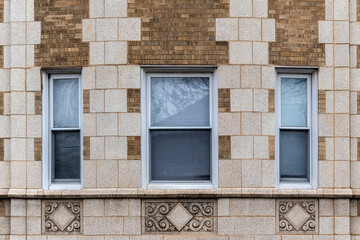 Fototapeta premium Three rectangular windows on a brick wall clad in beige tiles, with bas-reliefs beneath the windows. From the Windows of the world series.