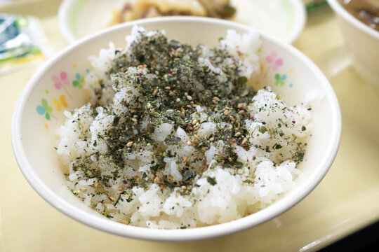A bowl of white rice topped with furikake seasoning served in Japanese school lunch